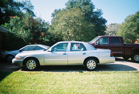 2000 Ford Crown Victoria - A silver sedan is parked in front of a maroon pickup truck on a sunny day.