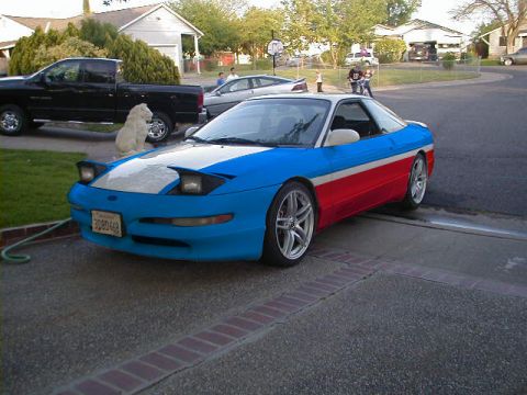 1997 Ford Probe - Front three-quarter view of a hatchback coupe in a blue, white and red paint scheme parked in a residential driveway, with pop-up headlight…