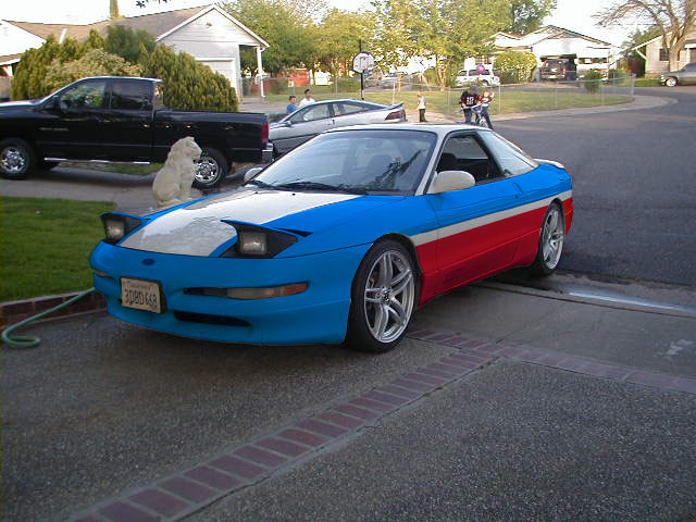 Blue, white and red painted coupe with pop-up headlights raised in a residential driveway
