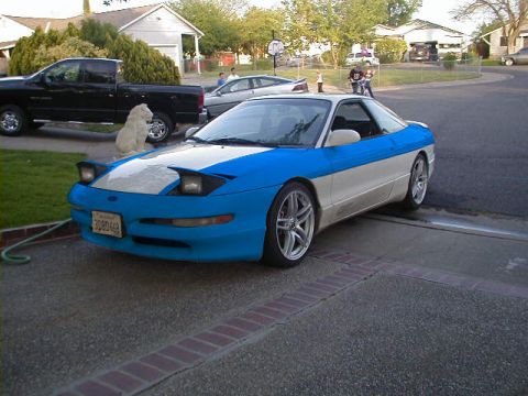 1997 Ford Probe - A two-tone Ford Probe is parked in a suburban driveway next to a pickup truck and a dog.