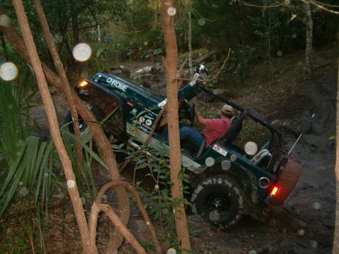 1991 Ford Bronco - A green Jeep Wrangler tackles a challenging muddy trail, with "CHROME" visible on its roof.