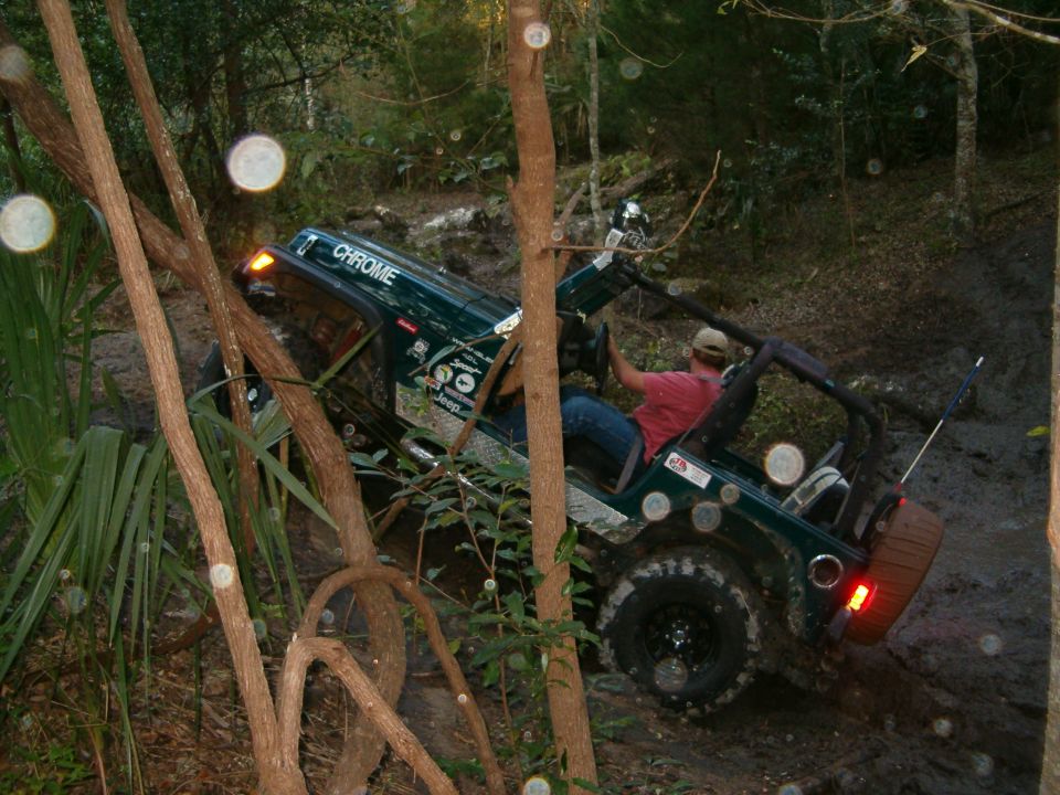 Green Jeep Wrangler with "CHROME" text on roof, navigating muddy terrain