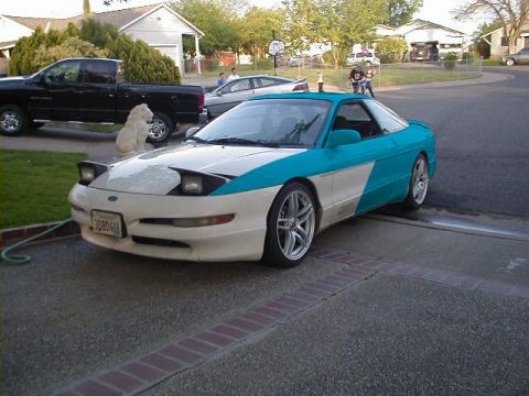 1997 Ford Probe - A two-tone white and teal sports car is parked in a driveway next to a black pickup truck.