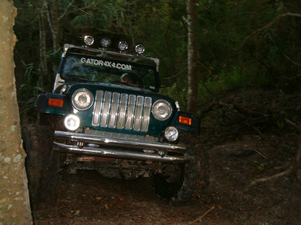 Green Jeep Wrangler with GATOR4X4.COM sticker on windshield, driving on a dirt trail