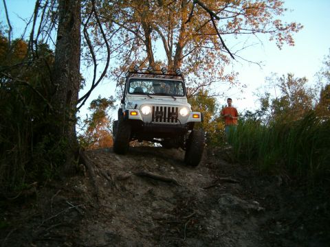 1991 Ford Bronco - White Jeep Wrangler TJ navigates an off-road trail with a person observing from the side.