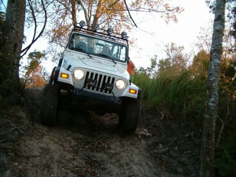 1991 Ford Bronco - A white Jeep Wrangler navigates an off-road trail, its front-left tire elevated on a steep incline.