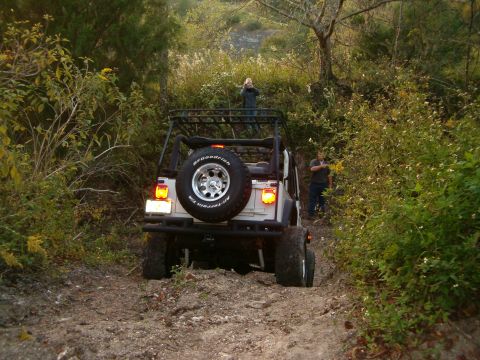 1991 Ford Bronco - A Jeep navigates a wooded trail with two people observing the off-road adventure.