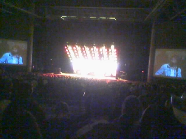 Concert stage with bright lights and two large screens showing a performer