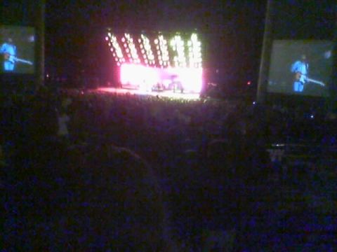 1986 Ford Bronco - A concert scene with a brightly lit stage and large screens displaying performers, seen from the audience.
