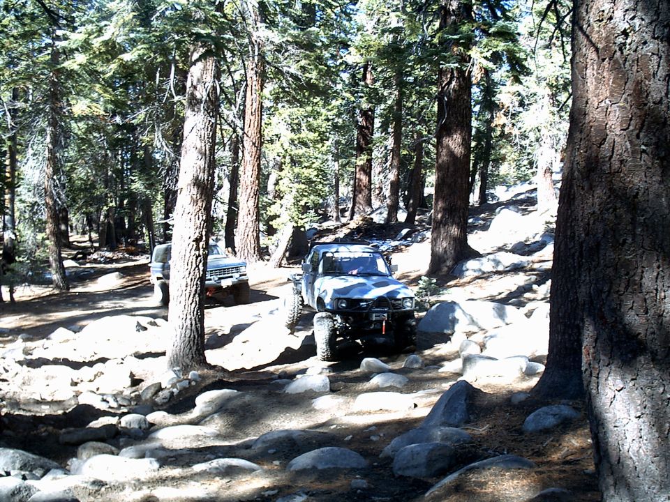 Two off-road vehicles on a rocky, wooded trail