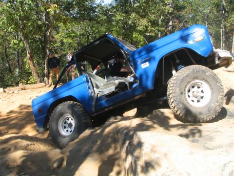1990 Ford Bronco - This blue Ford Bronco is navigating a rocky off-road course with its doors open.