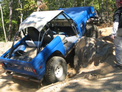 1990 Ford Bronco - A blue off-road vehicle navigates a rocky trail, with another vehicle visible in the background.
