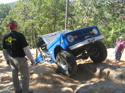 1990 Ford Bronco - This blue Ford Bronco is navigating a challenging rocky terrain, with spectators watching the off-road action.