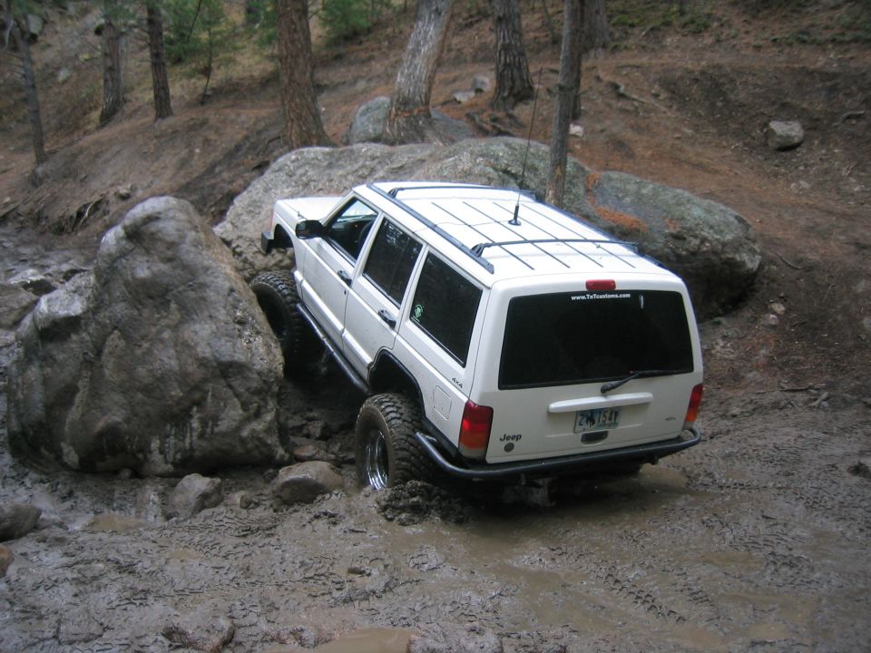 1997 Jeep Cherokee navigating a muddy, rocky trail with large boulders