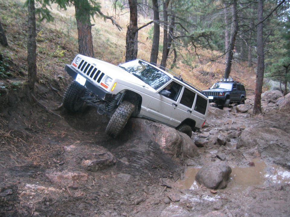 Silver 1997 Jeep Cherokee on a rocky, muddy trail, with a black Jeep Cherokee behind it