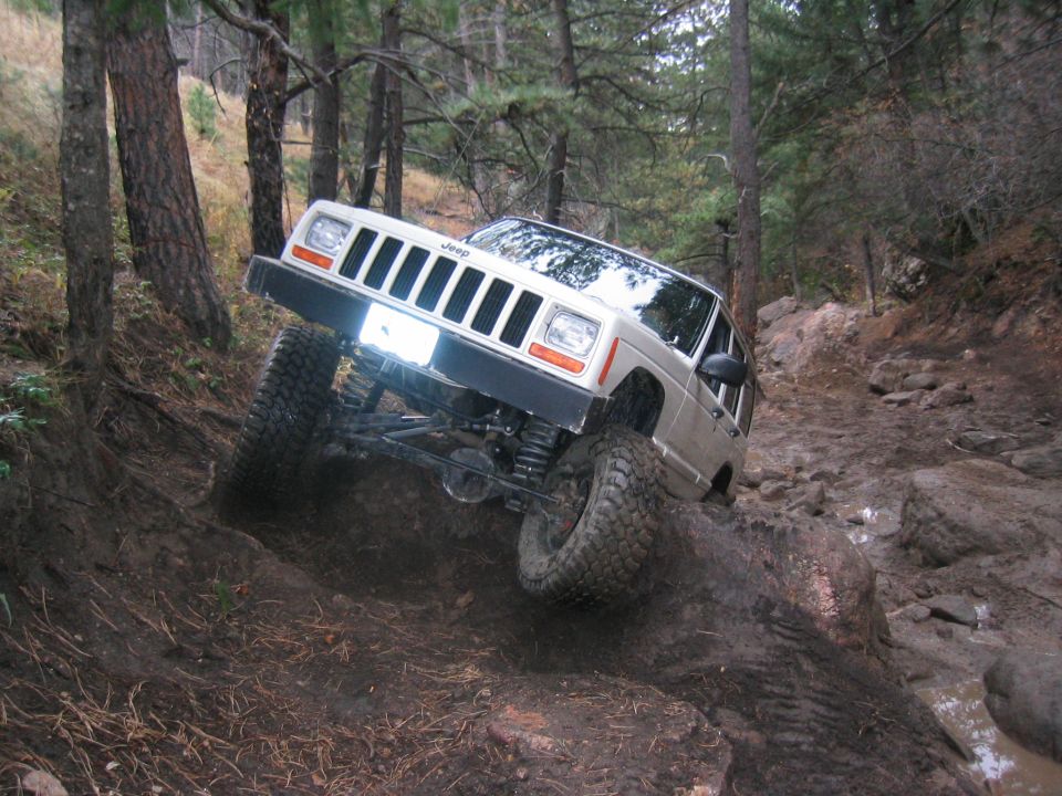 Jeep Cherokee climbing a muddy, rocky trail with trees on either side