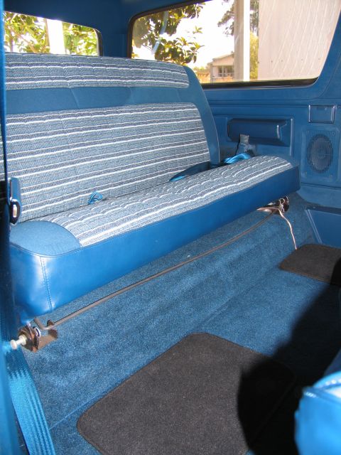 1984 Ford Bronco - The interior of a vehicle shows a blue rear seat with a striped pattern and matching blue carpet.