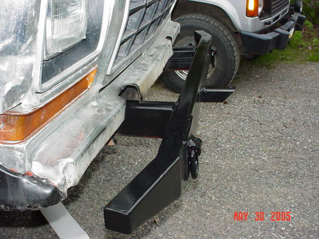 Fabricated black steel front bumper with shackle tab lying on gravel beside a truck
