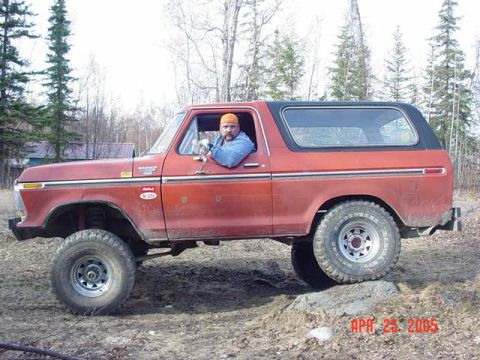 1978 Ford Bronco - Man driving a red 1978 Ford Bronco on a dirt path with trees in the background.