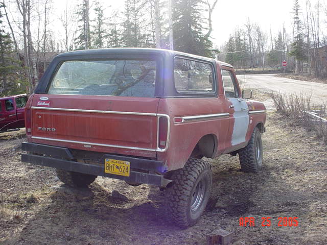 Red 1978 Ford Bronco with a black roof and bumper, parked on a dirt road