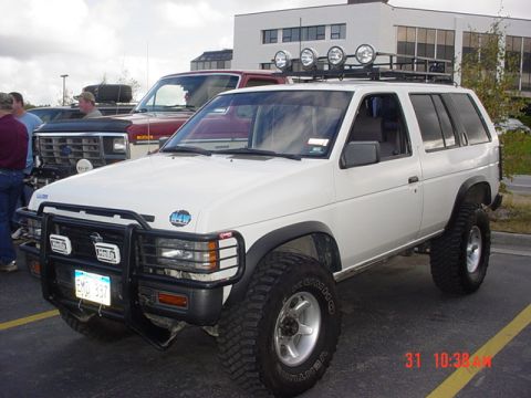 1976 Jeep CJ7 - A white SUV with off-road modifications is parked in a lot, with other vehicles visible in the background.