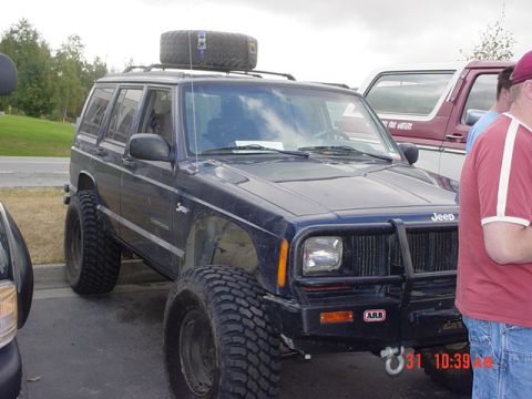 1976 Jeep CJ7 - A dark blue Jeep Cherokee XJ is parked next to another vehicle, with a spare tire mounted on its roof rack.