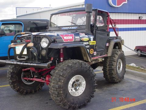 1976 Jeep CJ7 - Modified black Jeep CJ with prominent off-road tires and accessories is parked next to a blue vehicle.