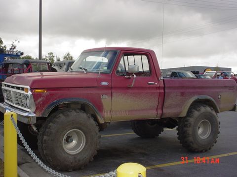 1976 Jeep CJ7 - This red Ford F-150 pickup truck features large off-road tires and shows signs of recent use with mud splatter on its body.