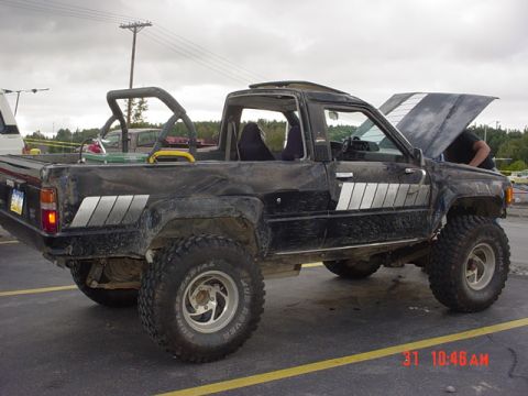 1976 Jeep CJ7 - Modified black pickup truck with off-road tires and an open hood.