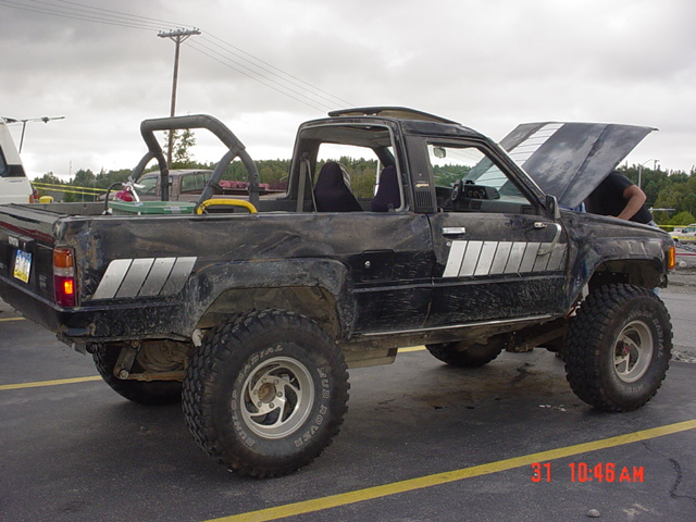 Black pickup truck with roll bar, lifted suspension, and off-road tires. Hood is open with a person underneath