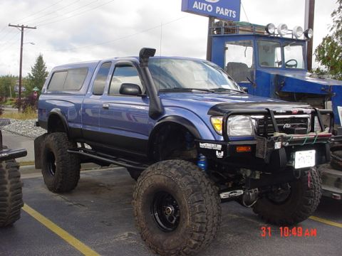 1976 Jeep CJ7 - A modified blue pickup truck with a snorkel and oversized tires is parked in front of a blue utility vehicle.