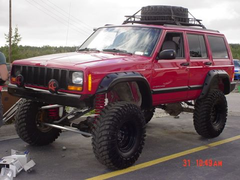 1976 Jeep CJ7 - This lifted red Jeep Cherokee features oversized tires, a roof rack with a spare tire, and custom off-road lights.