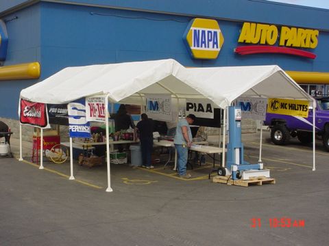 1976 Jeep CJ7 - An outdoor event is set up in front of a NAPA Auto Parts store, tents and a purple lifted truck.