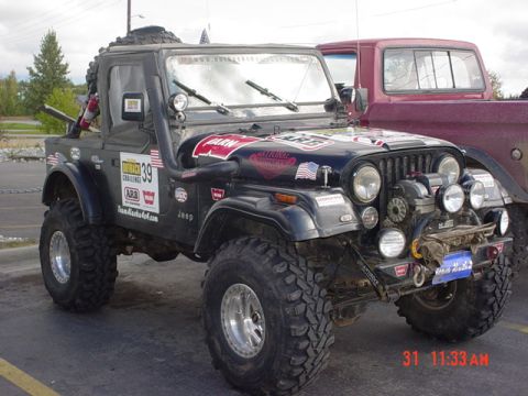 1976 Jeep CJ7 - A modified 1976 Jeep CJ7 is parked next to a red pickup truck, adorned with various racing decals.