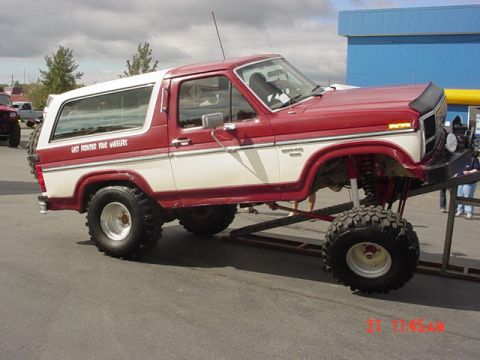 1976 Jeep CJ7 - A modified red and white Ford Bronco is displayed on a platform at an outdoor event.