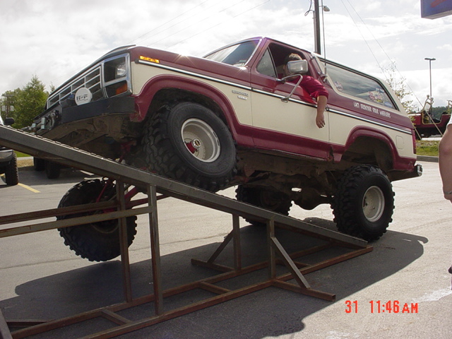 Red and white lifted 1980 Ford Bronco on a ramp, front grille visible
