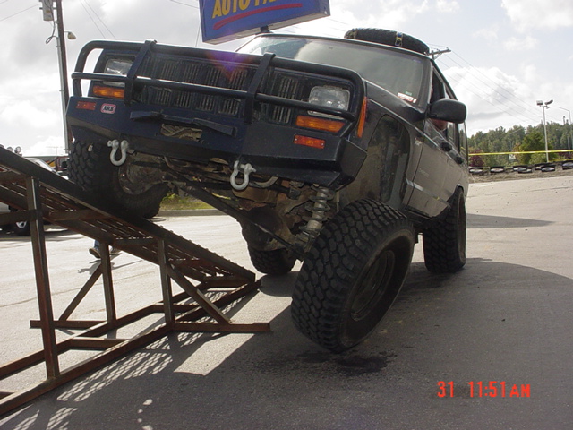 Black Jeep Cherokee XJ with aftermarket bumper and winch on a metal ramp