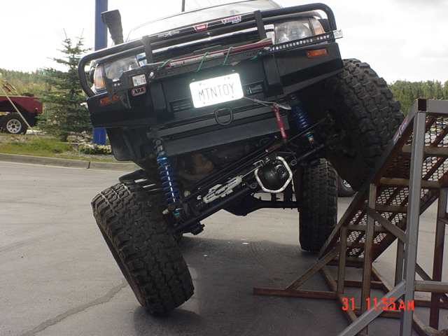 Black modified SUV with large tires and suspension, angled on a ramp
