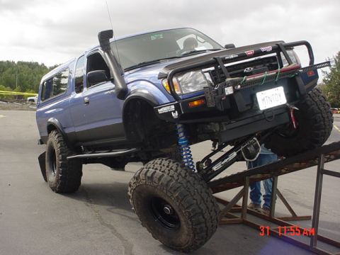 1976 Jeep CJ7 - Modified blue Toyota Tacoma with snorkel and off-road bumper is shown on a ramp.
