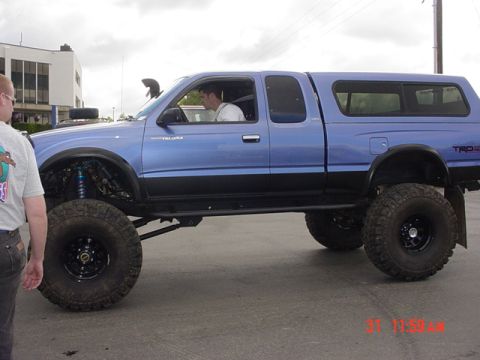 1976 Jeep CJ7 - A modified blue Toyota Tacoma pickup truck with a camper shell is shown from the side.