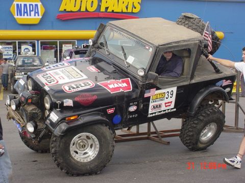 1976 Jeep CJ7 - Modified 1976 Jeep CJ7 with numerous decals and off-road lights, parked outside a NAPA Auto Parts store.