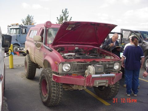 1976 Jeep CJ7 - Modified red Toyota pickup truck with snorkel and winch, hood open. Another truck is visible in the background.