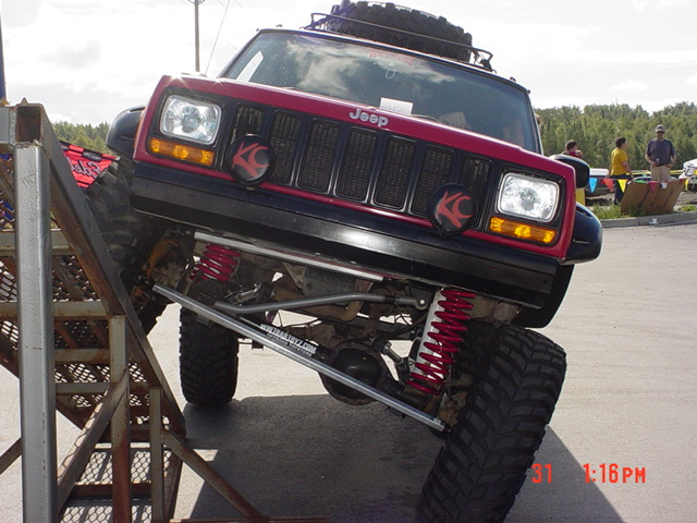 Red Jeep Cherokee XJ with off-road suspension on a metal ramp