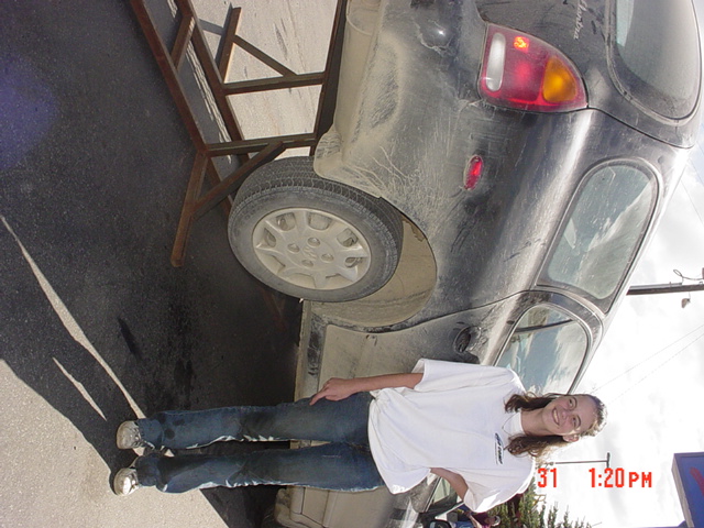Black hatchback with a person standing next to it, rear quarter view. Date stamp shows 1:20 PM