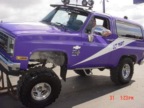 1976 Jeep CJ7 - A man is driving a lifted purple Chevrolet K5 Blazer with "Got Mud?" text on the side.