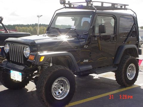 1976 Jeep CJ7 - A black Jeep Wrangler TJ is parked on asphalt with a roof rack and off-road tires visible.