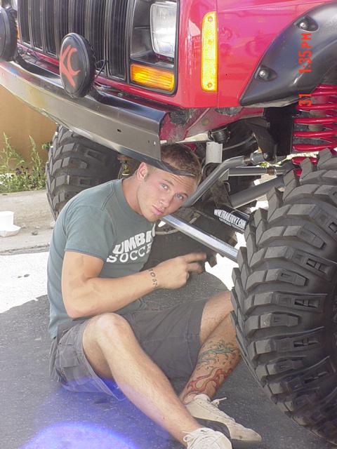 1976 Jeep CJ7 - Man works on a red Jeep, possibly a CJ7, with custom modifications and large off-road tires.