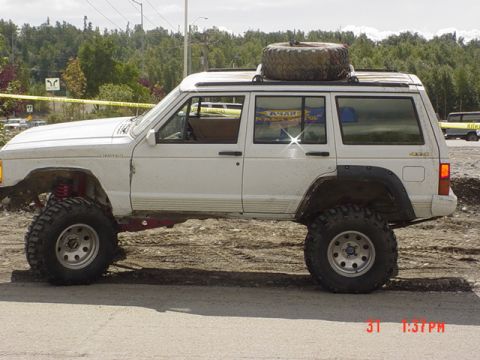 1976 Jeep CJ7 - Modified white Jeep Cherokee XJ with off-road tires and a roof-mounted spare tire is shown from the side.