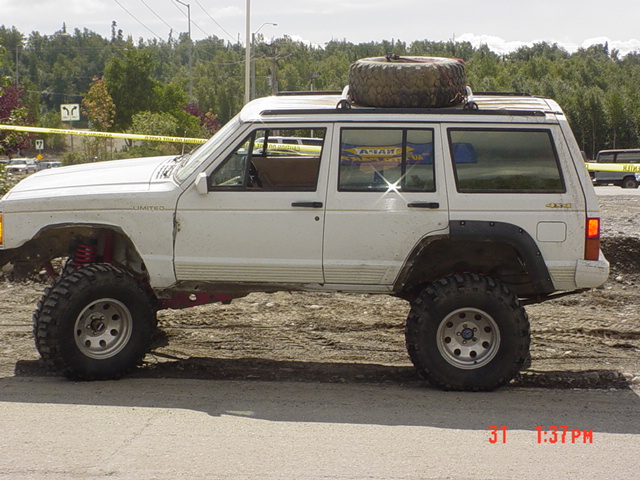 White Jeep Cherokee XJ with lifted suspension and large tires, spare tire on roof rack
