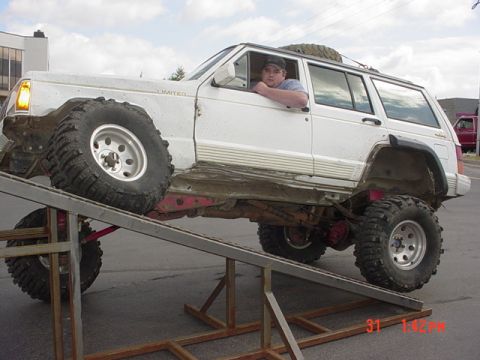 1976 Jeep CJ7 - A modified white Jeep Cherokee SUV is positioned on a metal ramp, with a person inside.